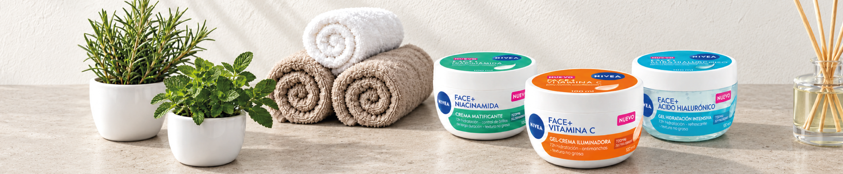Imagen de cuidado facial con una selección de cremas Nivea Face+ sobre una superficie de piedra en un entorno tipo spa. Incluye tratamientos con Niacinamida, Vitamina C y Ácido Hialurónico para hidratación, luminosidad y cuidado diario de la piel. Los productos aparecen acompañados de toallas enrolladas, plantas aromáticas y un difusor de varillas.