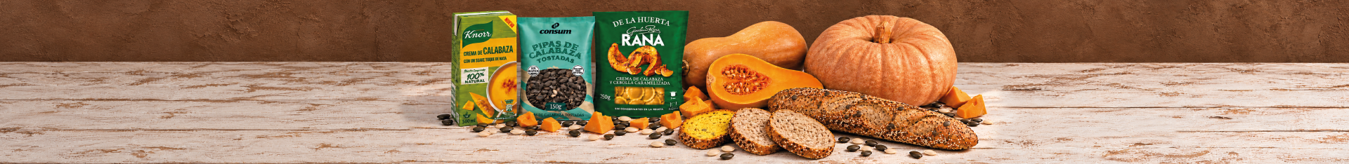 Imagen de productos elaborados con calabaza sobre una mesa de madera de estilo rústico. Incluye crema de calabaza Knorr, pipas de calabaza tostadas Consum y pasta rellena de calabaza y cebolla caramelizada Giovanni Rana, acompañadas de calabazas enteras y cortadas, pan de semillas, dados de calabaza y pipas de calabaza dispersas.
